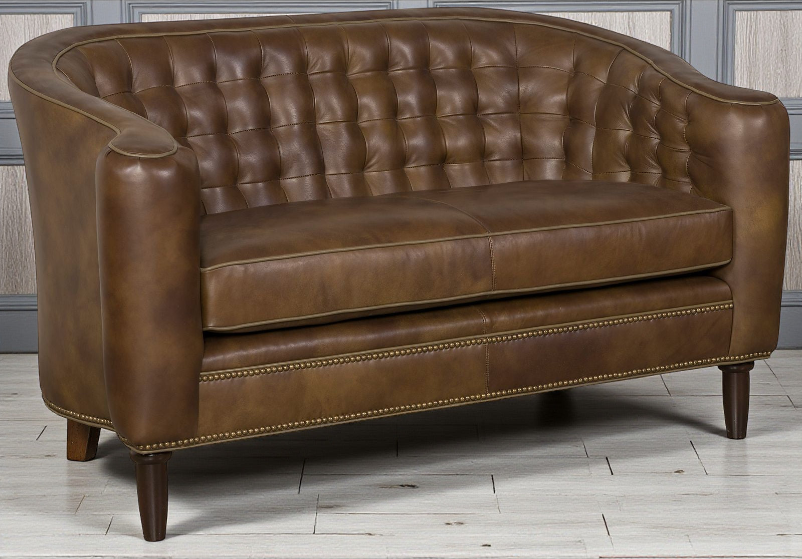 Brown leather loveseat with tufted backrest on a wooden floor.