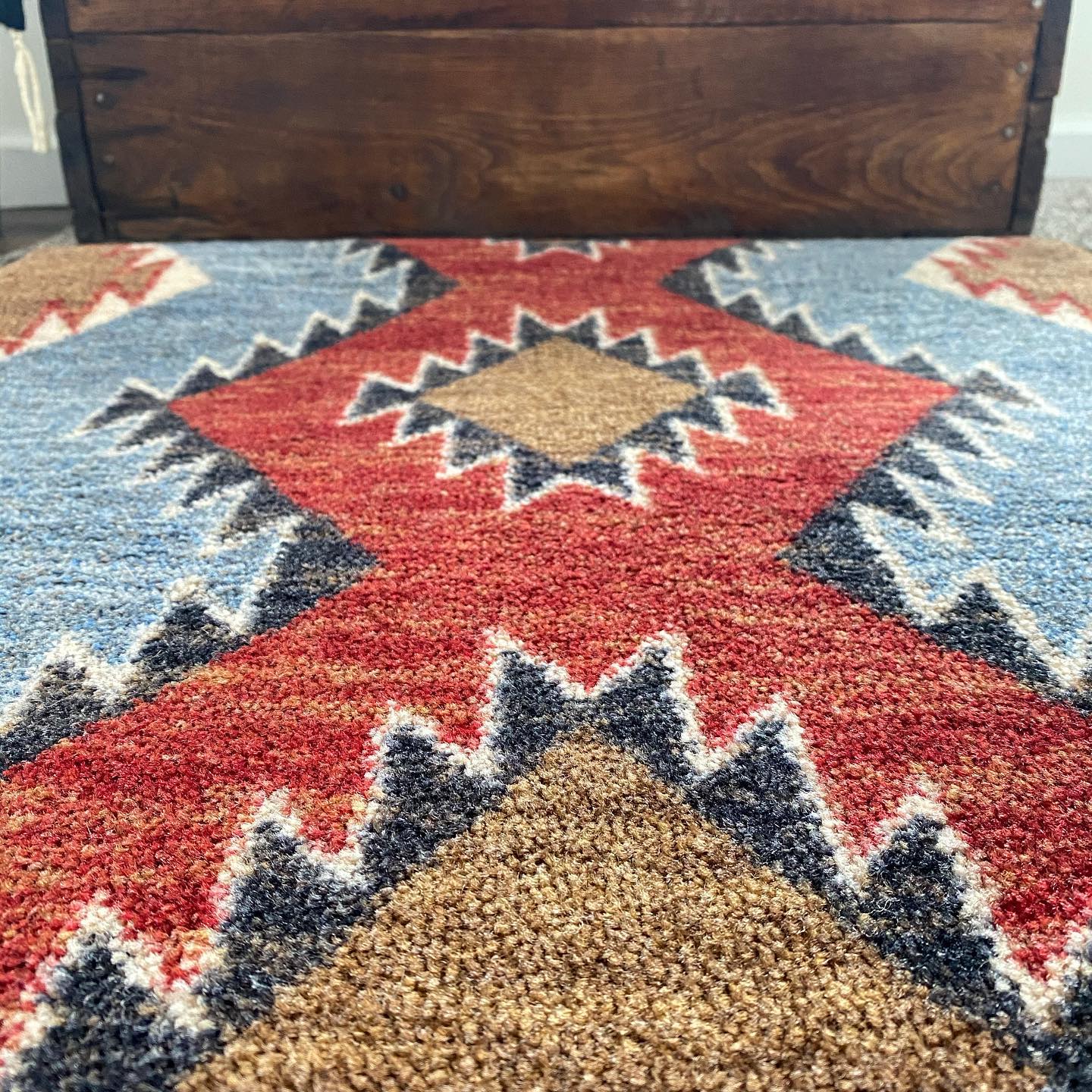 southwestern area rug with red, blue, and brown geometric diamond pattern on wood floor, western style performance rug detail 