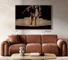 Brown leather sofa in a living room with a large painting of a bucking bull and rider on the wall - Your Western Decor